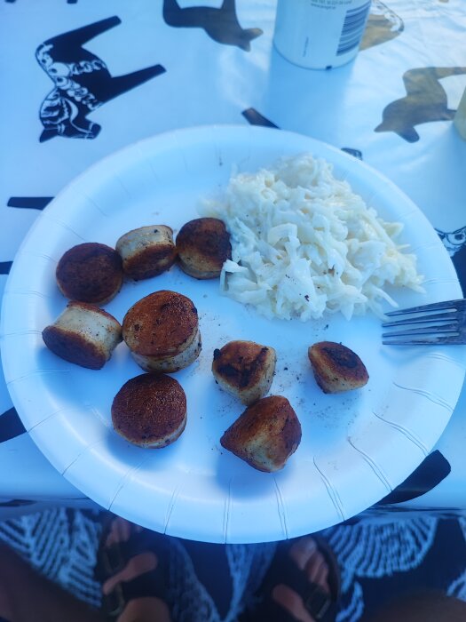 Pappersfat med skivade bratwurst och vitkålssallad på, placerat på ett bord med duk.