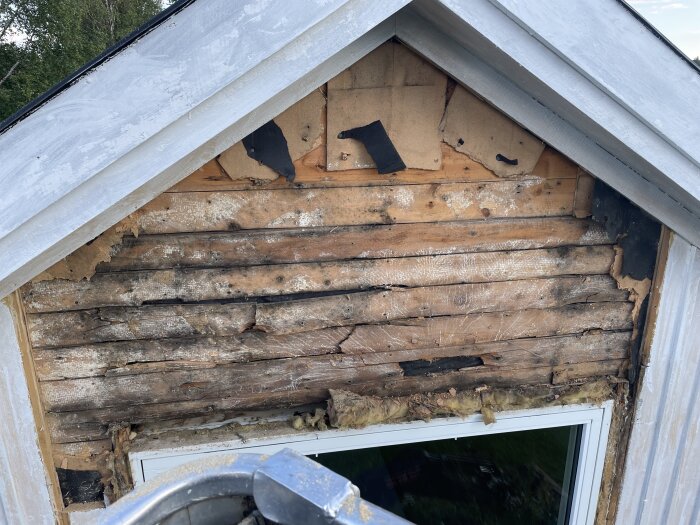 Utsatt del av yttervägg med synliga skador och mögel ovanför ett fönster på ett hus under renovering.