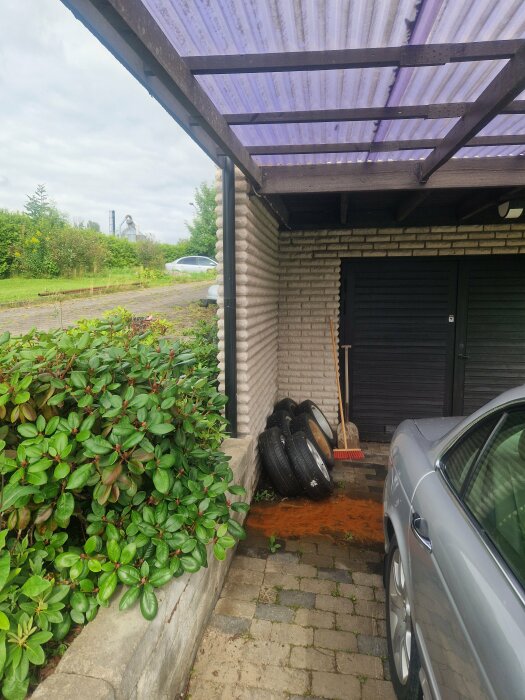 Läckage med kantarellgult sediment från grunden vid en carport, intill en grön buske och en hög med däck.