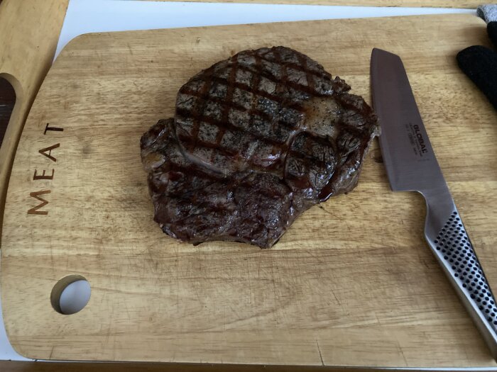 Grillad biff med grillränder ligger på en skärbräda bredvid en rostfri kökskniv.