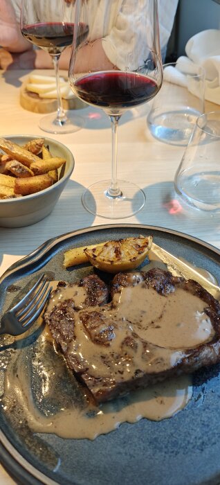 En tallrik med kött i sås, en grillad citron och rostad potatis, serverad med glas vin.