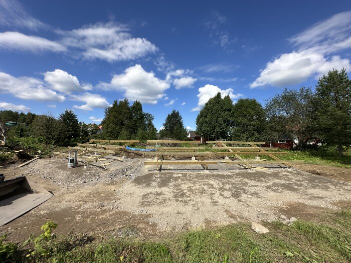 Markställning byggd för solpaneler på en gruslagd markyta, omgiven av grönska och byggnader i bakgrunden.