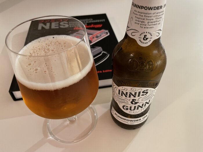 Flaska och glas med Gunnpowder IPA-öl från Innis & Gunn på ett bord, med en NES-bok i bakgrunden.