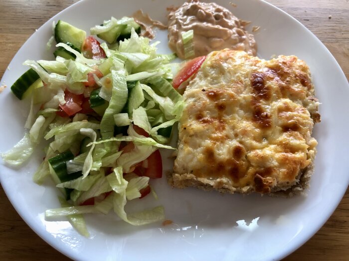 Räkoch-chilipaj serverad med sallad bestående av gurka, tomat och isbergssallad, samt en klick smaksatt crème fraîche på en vit tallrik.