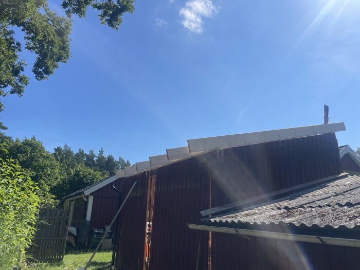 Byggprojekt med nylagda takreglar på ett rött hus under en klarblå himmel. Detaljer som gröna träd och en annan byggnad i bakgrunden.