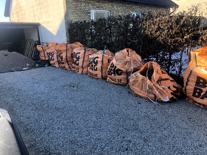 Sex stora Big Bags fyllda med jord och betong står uppradade på en grusbelagd uppfart framför ett tegelhus under renovering.