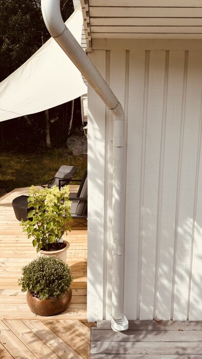 Vitt stuprör på vit fasad, trekantssegel över ny terrass med trädgårdsmöbler och krukväxter, förberett för 40-årsfest.