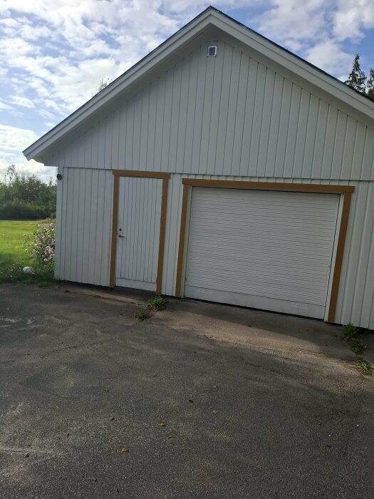 Vitt hus med dörr och garageport, tidigare sopskåp till vänster om dörren har tagits bort och väggen blivit panelad.