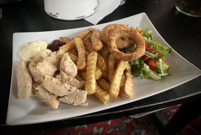 Tallrik med stekt kycklingfilé, pommes frites, sallad, två lökringar, majonnäs och BBQ-sås.