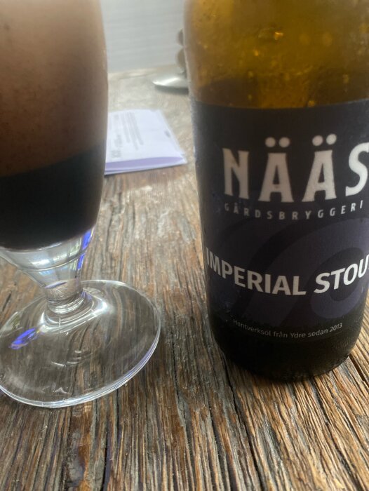 En flaska Nääs imperial stout och ett glas fyllt med drycken på ett träribbat bord.