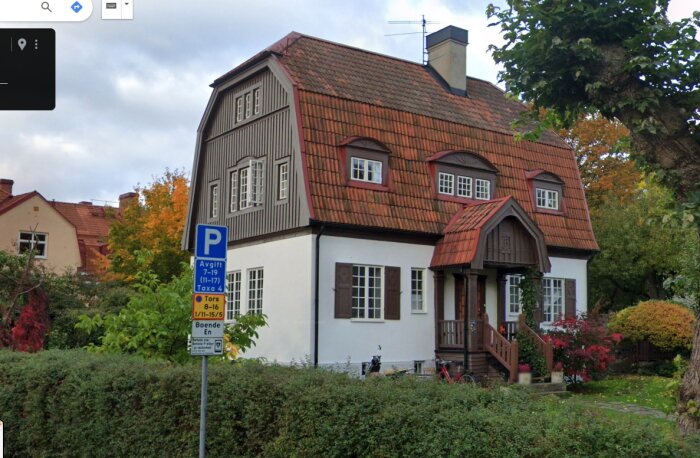 Vit villa med rött tak och takkupor i Gamla Enskede, Stockholm. Huset har högt tak och dubbelrader av fönster, och en parkering-skylt står framför.