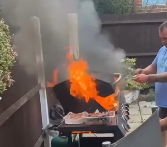 Man står bredvid en grill med stora flammor och rök som stiger, tydligen efter att ha använt felaktiga råd.