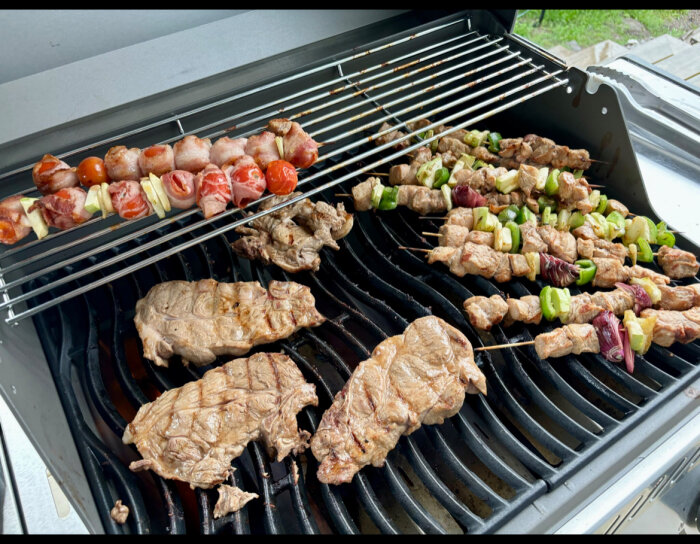 Grill med flera spett med olika sorters kött och grönsaker samt köttbitar, redo att grillas.