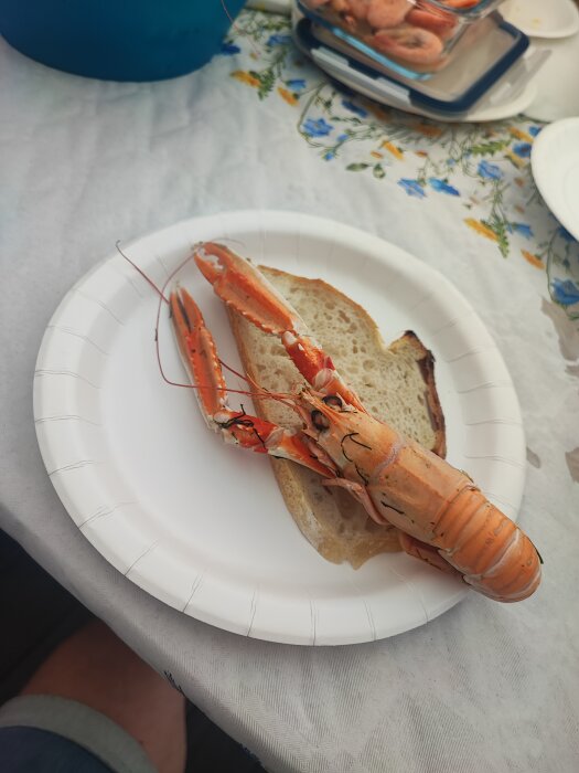 Kräfta på en papperstallrik tillsammans med en brödskiva, placerad på en bordsduk med blommönster.