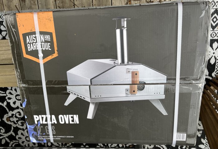 Förpackning av Austin and Barbeque 12" gasolpizzaugn, med bild på ugnens stålgrå design och skorsten, mot en mörk bakgrund.