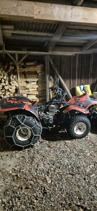 Suzuki LT-F 250 fyrhjuling utan kåpor, innan spackling och lagning, med snökedjor på bakhjulen, parkerad i en vedbod.