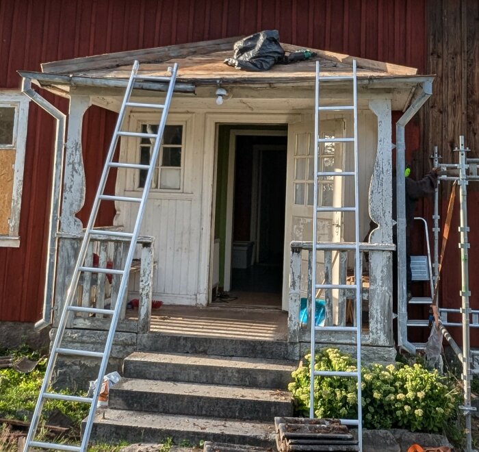 Entrétak med tre sidor i behov av renovering, två stegar lutade mot taket och gamla hängrännor. Delen av huset är röd med vit dörr och fönster.