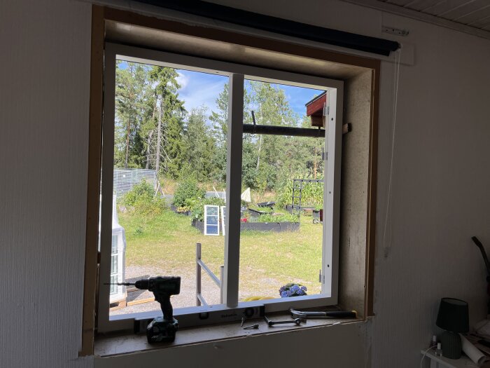 Byggprojekt med fönsterbyte, visar nytt fönster delvis installerat från insidan, olika verktyg som borrmaskin och vattenpass på fönsterbrädet.