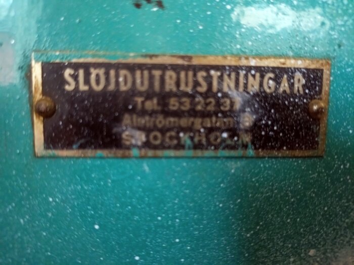 Närbild på en märkskylt på en bandsåg med texten "SLÖJDUTRUSTNINGAR" på en grön yta