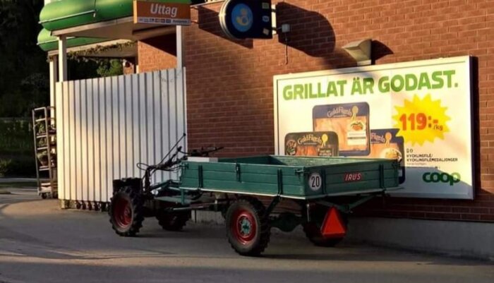 Grön vagn parkerad framför en Coop-annons som marknadsför grillad kycklingfilé för 119 kr/kg, vid en byggnad med ett uttagsautomat.