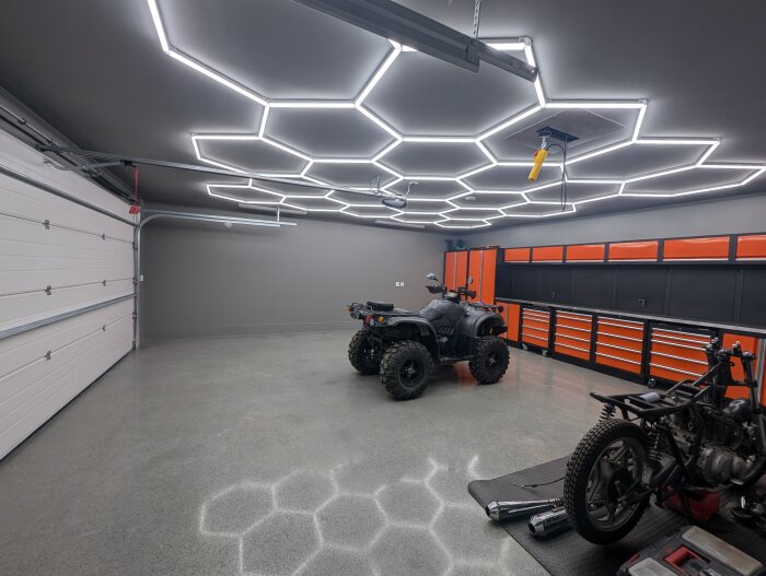 Garage med huvudbelysning installerad, hexagonformade LED-lampor i taket, samt en fyrhjuling och arbetsbänk med verktygsskåp.