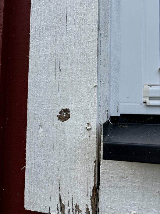 Närbild av vitmålad fasad med fönsterfoder och rötangripen sidobräda, med glipa mellan underbräda och sidobräda. Fönsterbleck syns till höger.