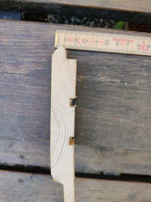 En närbild av en träpanelbit bredvid en tumstock som visar mätning i millimeter.