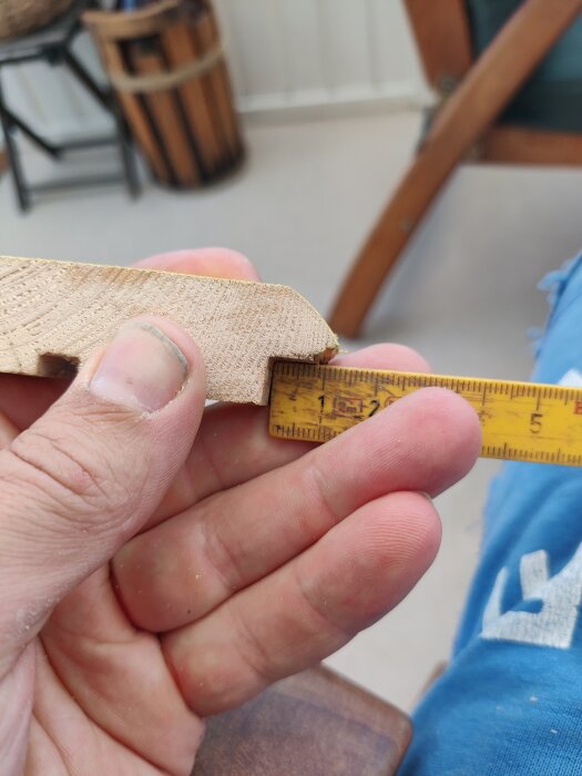 Hand som håller en bit träpanel bredvid ett måttband, troligtvis för att mäta tjockleken på panelen, på en byggarbetsplats.