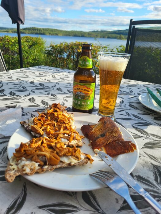 En tallrik med knäckebröd, smörstekta kantareller och nyrökt abborre, tillsammans med en flaska Sierra Nevada Pale Ale och ett glas öl, utomhus vid en sjöutsikt.