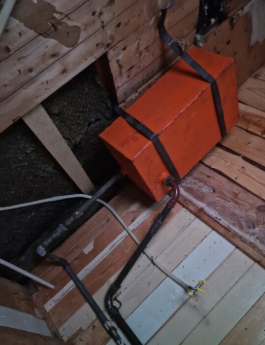 Orange rektangulär tank med röranslutningar, upptäckt i ett badrumsinnertak under en renovering. Omgivande träpanel är på väg att rivas.