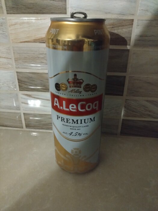 En burk A. Le Coq Premium lageröl med 4,5% vol alkoholhalt stående på en köksbänk med kakelvägg i bakgrunden.