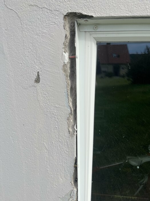Putsskadad vägg runt ett fönster i en källare. Putsen på väggen har lossnat, vilket visar underliggande material och eventuell skadad konstruktion.