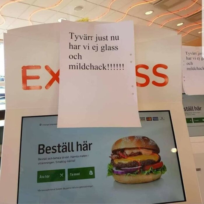 En lapp med texten "Tyvärr just nu har vi ej glass och mildchack!!!!!!" sitter ovanför en skärm för beställning i en snabbmatsrestaurang.