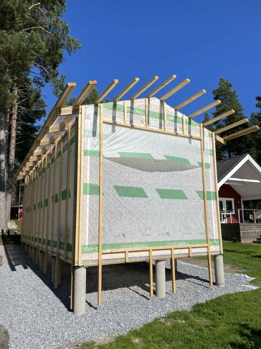 Byggnad med installerade spikläkt och musband, redo för panelmontering, omgiven av skog och gräs.