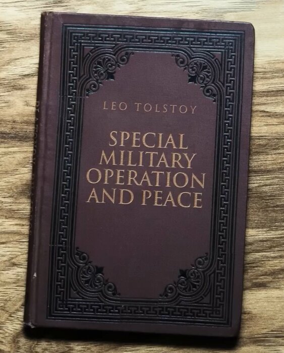 En bok med titeln "Special Military Operation and Peace" av Leo Tolstoy ligger på ett träbord. Omslaget är mörkt med dekorativa mönster.