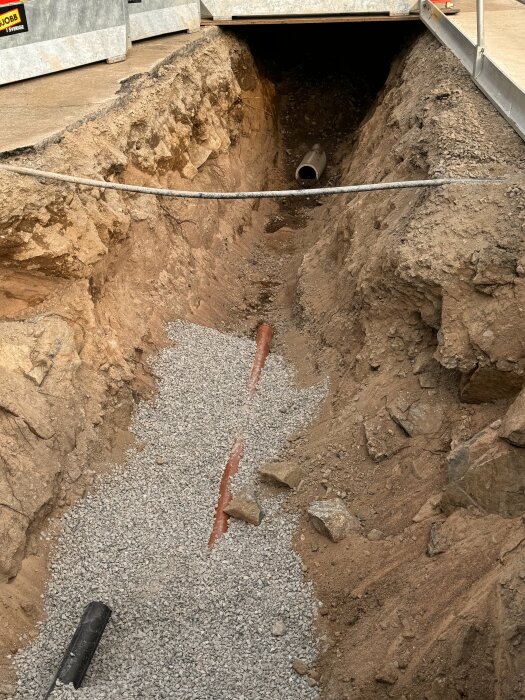 Utgrävd rörgrav fylld med makadam istället för sand, med ett synligt rör.