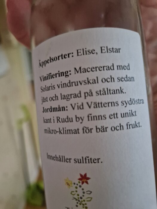 Närbild av etiketten på en flaska äppelvin från Rudu Vingård med information om äppelsorter, vinifiering och jordmån vid Vätterns sydöstra kant.