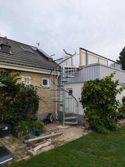 Nyinstallerad spiraltrappa från Hornbach som leder upp till en takterrass på ett hus med tegelfasad och solpaneler på taket.