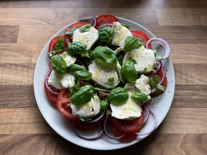 En tallrik med tomat- och mozzarellasallad, toppad med basilika, rödlök, olivolja och svartpeppar.