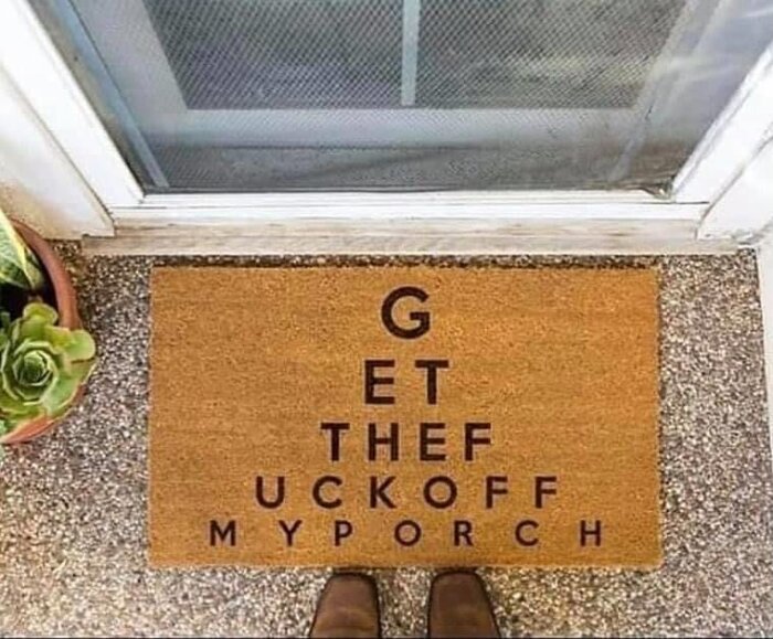 Dörrmatta med texten "Get the fuck off my porch" bredvid en krukväxt utanför en ytterdörr.