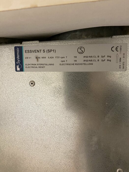 Närbild på en silverfärgad spiskåpa med etiketten "Systemair ESSVENT S (SP1)" som visar elektriska specifikationer och certifieringar.