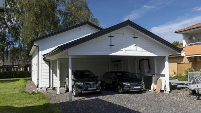 Nyrenoverad vit byggnad med nymålade vindskivor i mörk färg och två bilar parkerade under carport.