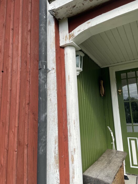 Närbild på ett hus från 1840-talet med fasad målad i röd slamfärg, vitmålade hörn och fönsterfoder som har spruckit färg, samt en grönmålad ytterdörr.