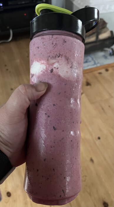 En hand håller i en sportflaska fylld med en rosa milkshake eller smoothie, gjord på jordgubbar, blåbär, mjölk och vaniljglass.