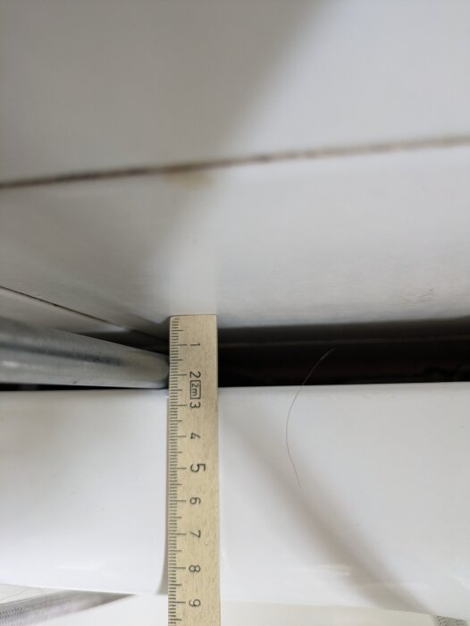 Linjal som mäter ett glapp på cirka 3 cm mellan ett badkar och en vägg.