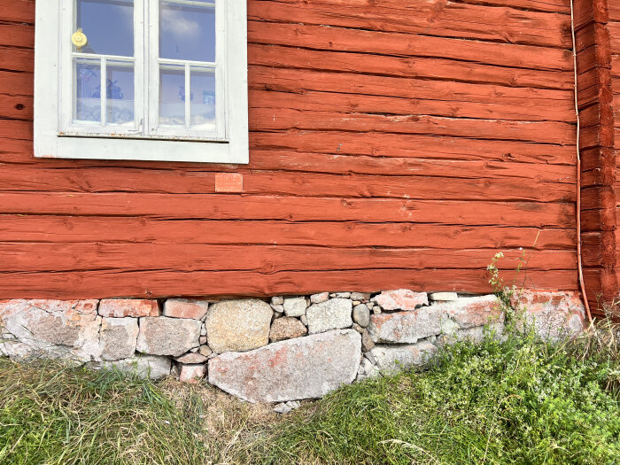 Stengrund på gammalt rött trähus där stora och små stenar återplacerats i den delvis raserade grunden.