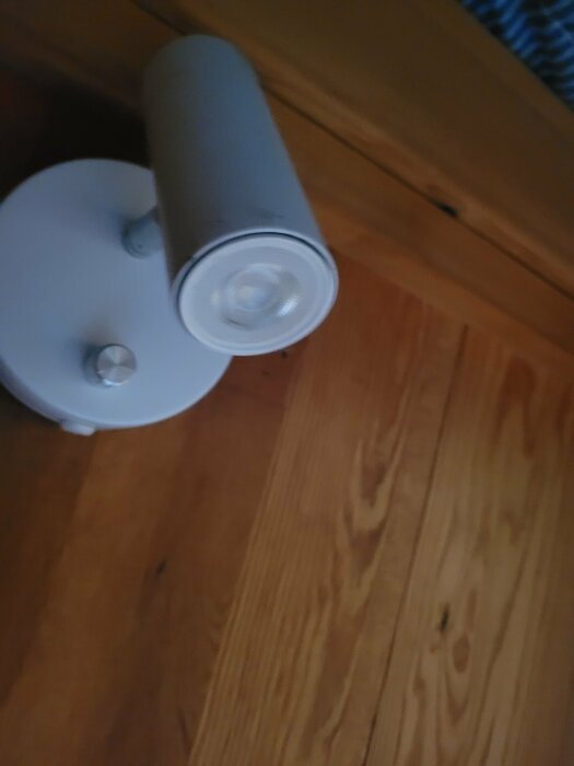 Vit väggmonterad spotlight-lampa på en träpanelvägg.