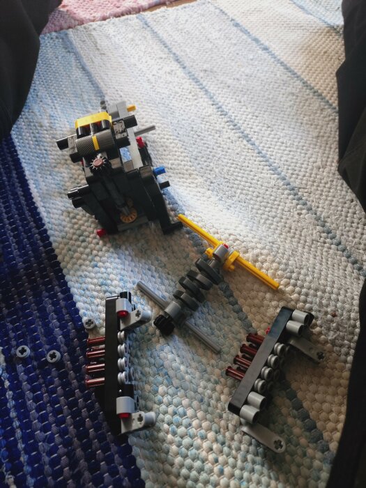 En påbörjad Lego-bil ligger på en randig matta med ben synliga i bakgrunden.