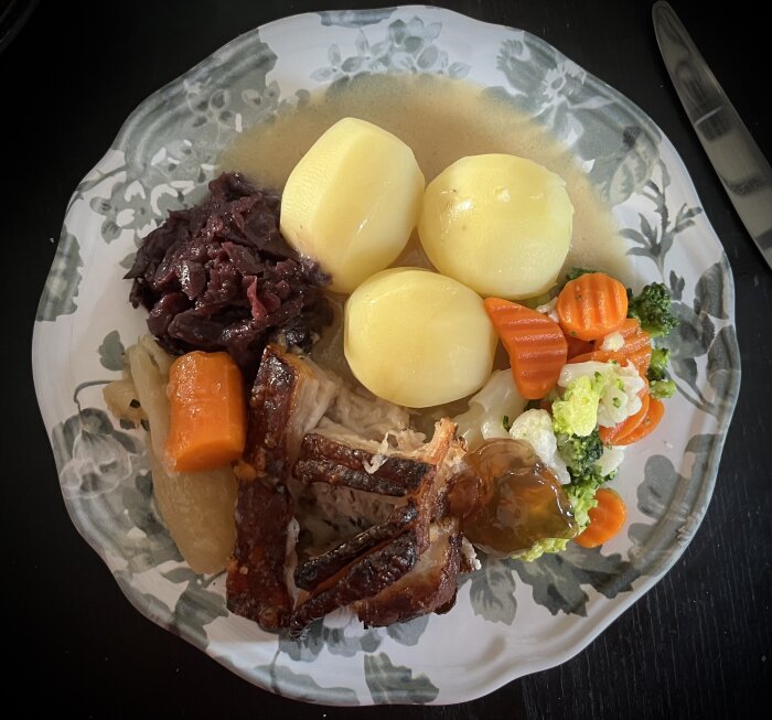 Tallrik med dansk fleskestej med krispig yta, kokt potatis, rödkål, kokta grönsaker (morötter och broccoli), sås och en klick äppelgelé.