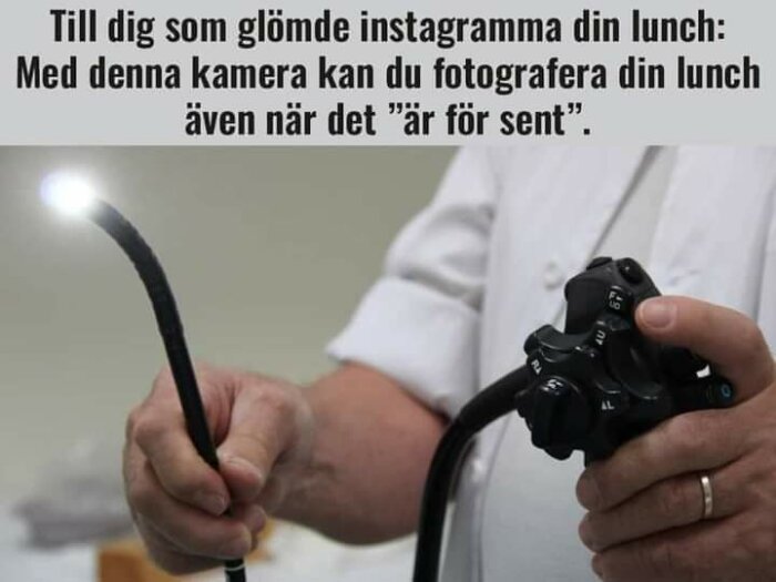 En person håller en endoskopikamera med en lysande spets och en kontrollenhet. Text ovanför: "Till dig som glömde instagramma din lunch: Med denna kamera kan du fotografera din lunch även när det är för sent".